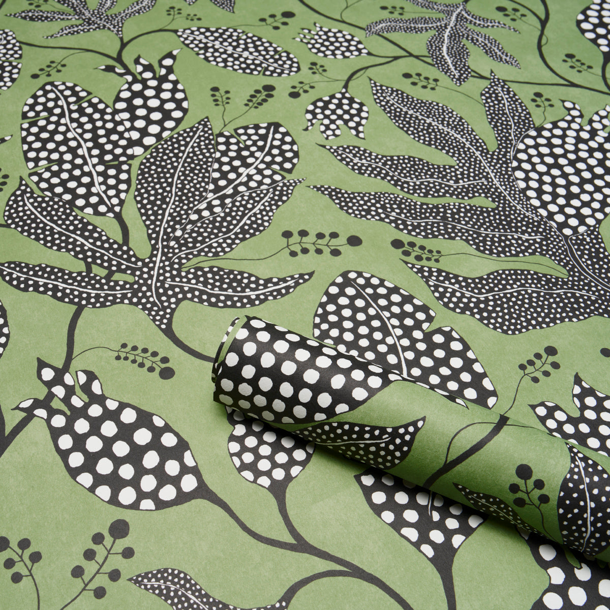 Green fabric with black and white botanical leaf print; rolled corner reveals dotted reverse.