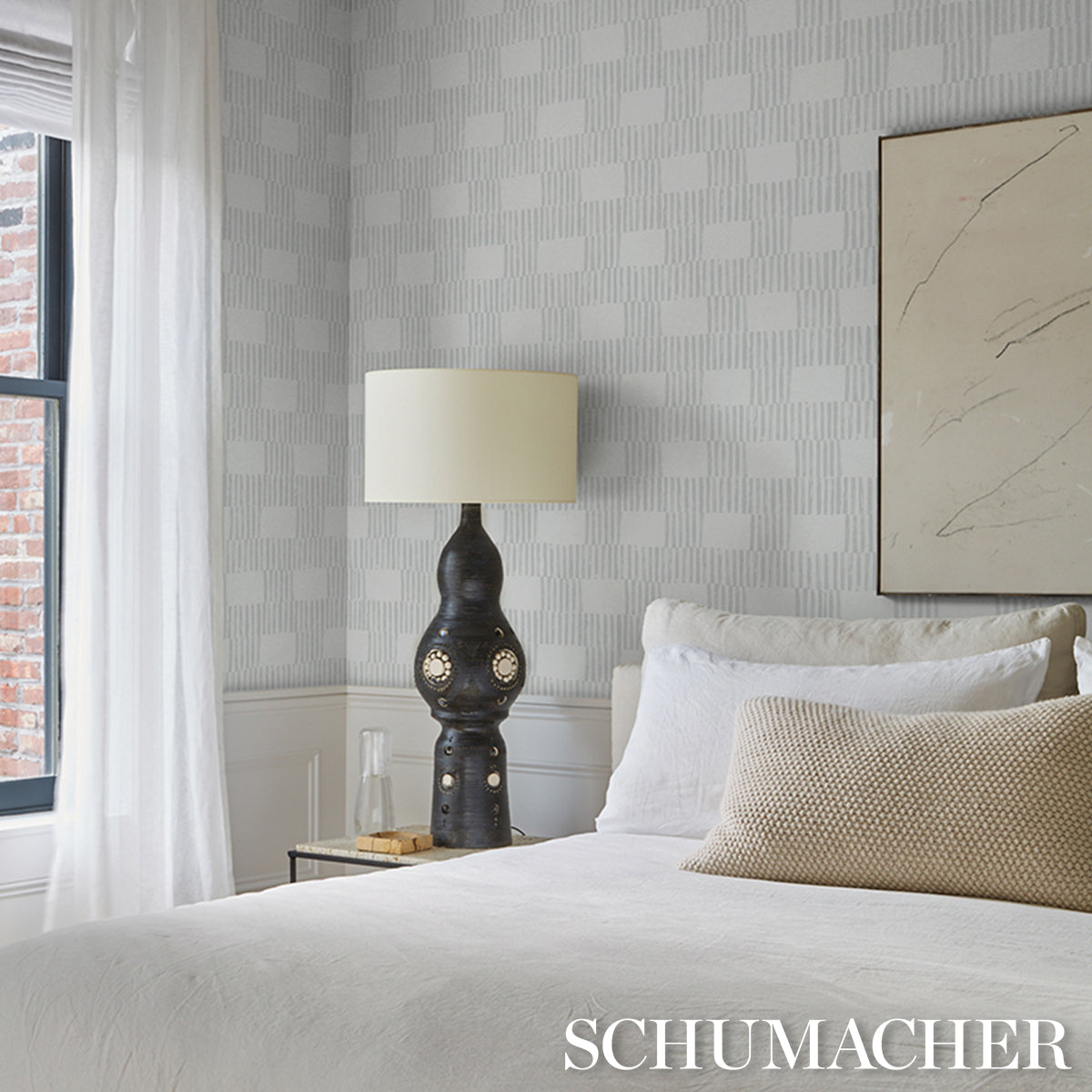 Bedroom with white bedding, beige cushion, ornate black lamp, glass side table, light gray patterned wallpaper.