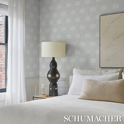 Bedroom with white bedding, beige cushion, ornate black lamp, glass side table, light gray patterned wallpaper.