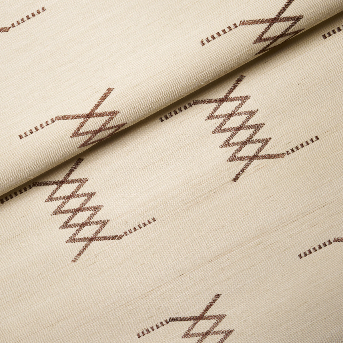 Beige sisal embroidery fabric with hazel on ivory geometric diamond pattern; folded edge, soft textile texture.