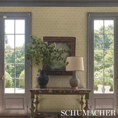 Dark carved wood console with beige lamp, blue vase of greenery, ornate mirror, and yellow geometric wallpaper.