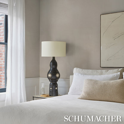 Dark ceramic table lamp with gold-tone circular cutouts and a cream shade on a nightstand in a neutral-toned bedroom.