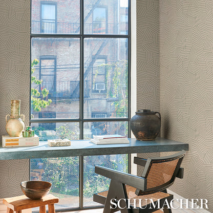 Industrial home office scene: gray desk by a large window, woven chair, ceramic vases, dark pot, books, wooden bowl, geometric wallpaper.