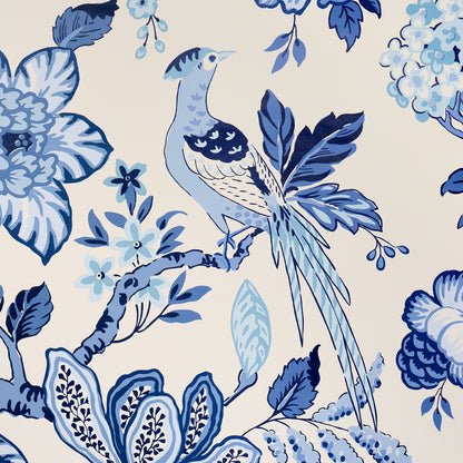 Blue and navy bird perched among stylized cream flowers and leaves in a toile-style fabric print.