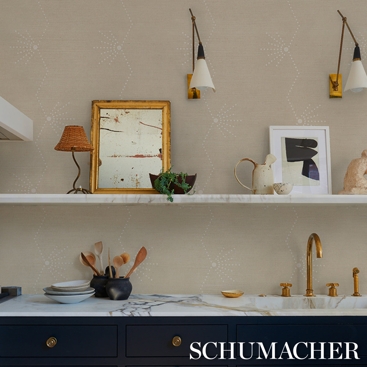 Beige patterned kitchen with white shelf, brass faucet, navy cabinets, marble countertop, framed art and decorative items.