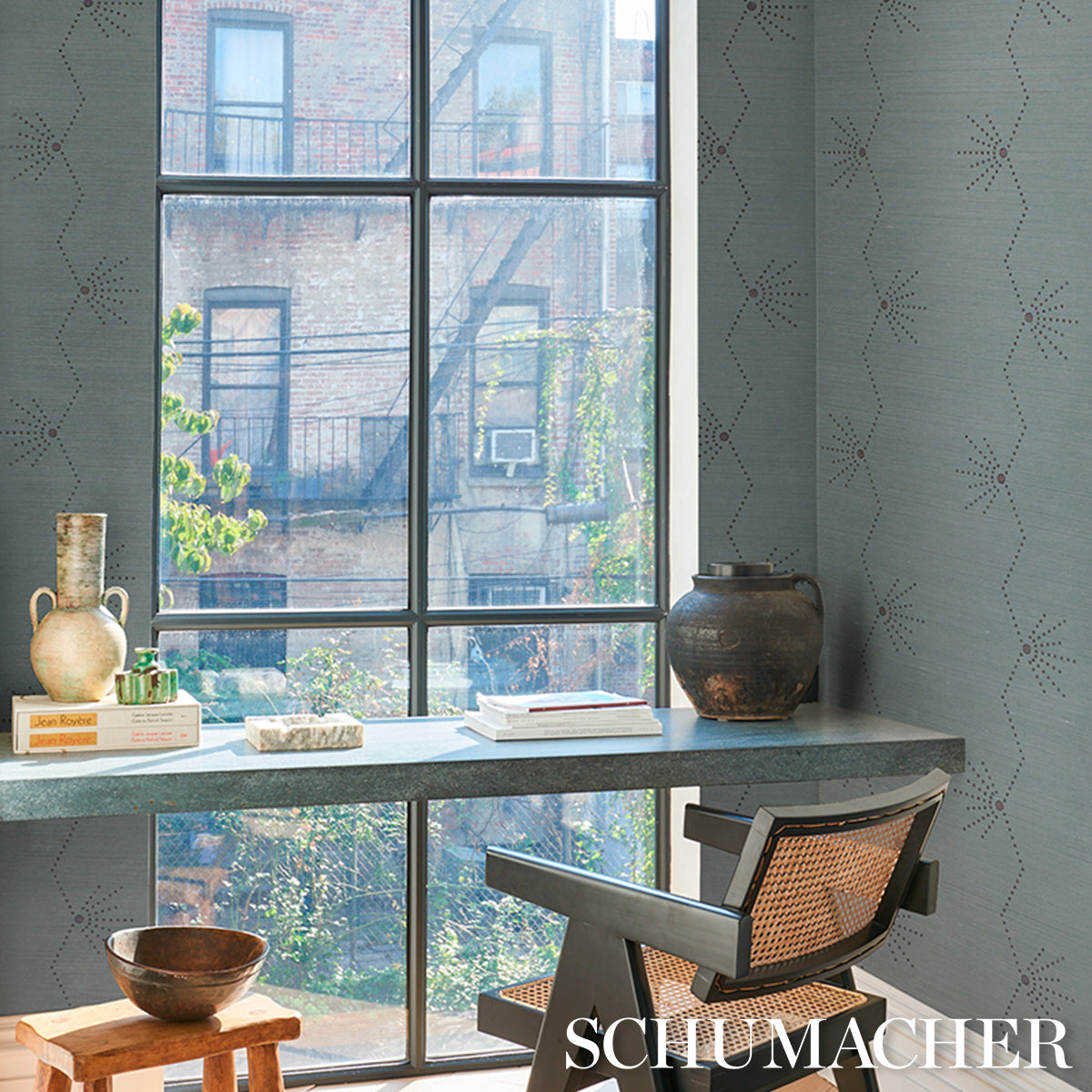 Cozy study nook by a large window with gray patterned walls, a desk, mid-century chair, ceramic jug, books, and clay pot.