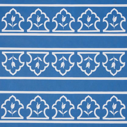 Blue background with white repeating border motifs, fleur-de-lis leaf shapes in arched panels across horizontal stripes.