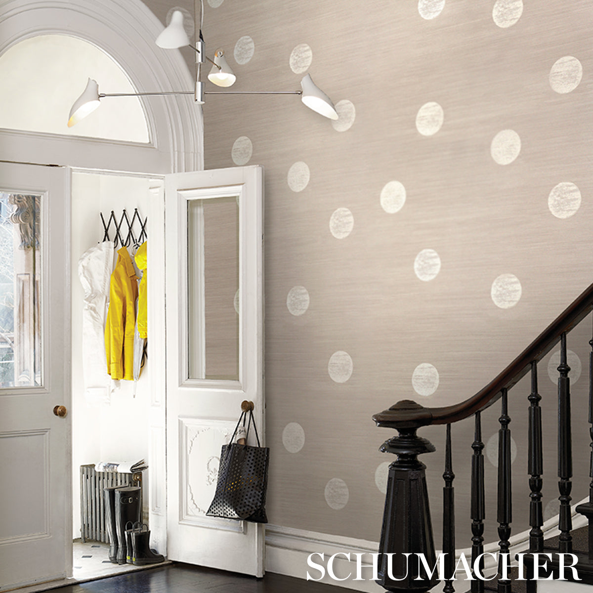 Entry hall with beige polka-dot wallpaper, white doors, dark wood railing, modern light fixture, yellow coat hanging.