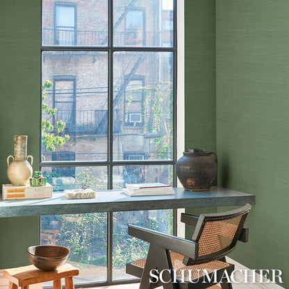 Green-walled sunlit home office; long gray stone-top desk, woven rattan chair, ceramic vases, books, clay pot by window.