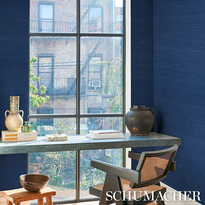 Blue-walled home office with a large window, gray stone desk, metal-framed woven chair, ceramic vase, and books.