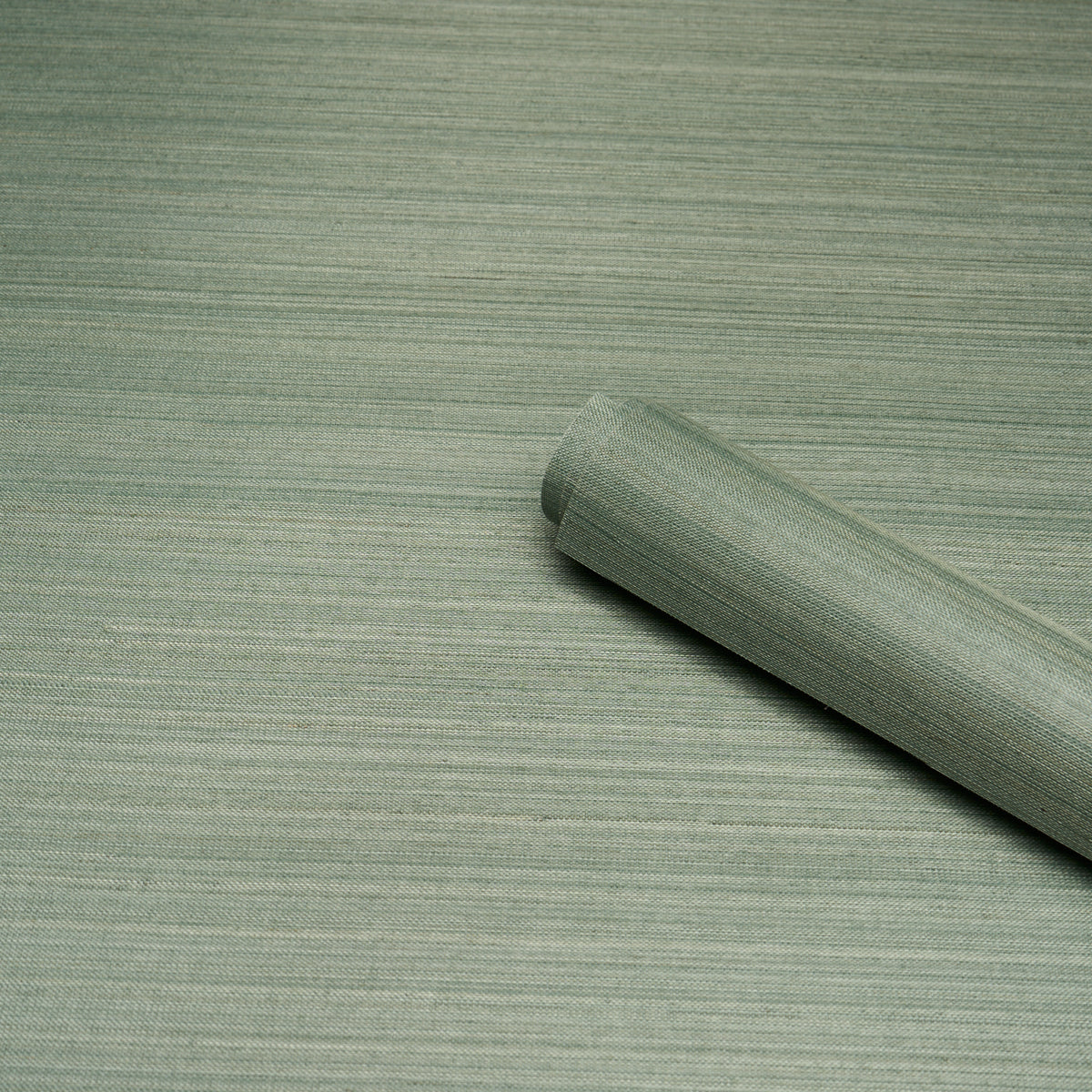 Light sage green wallpaper roll with linen-like texture, partially rolled on a matching green backdrop.