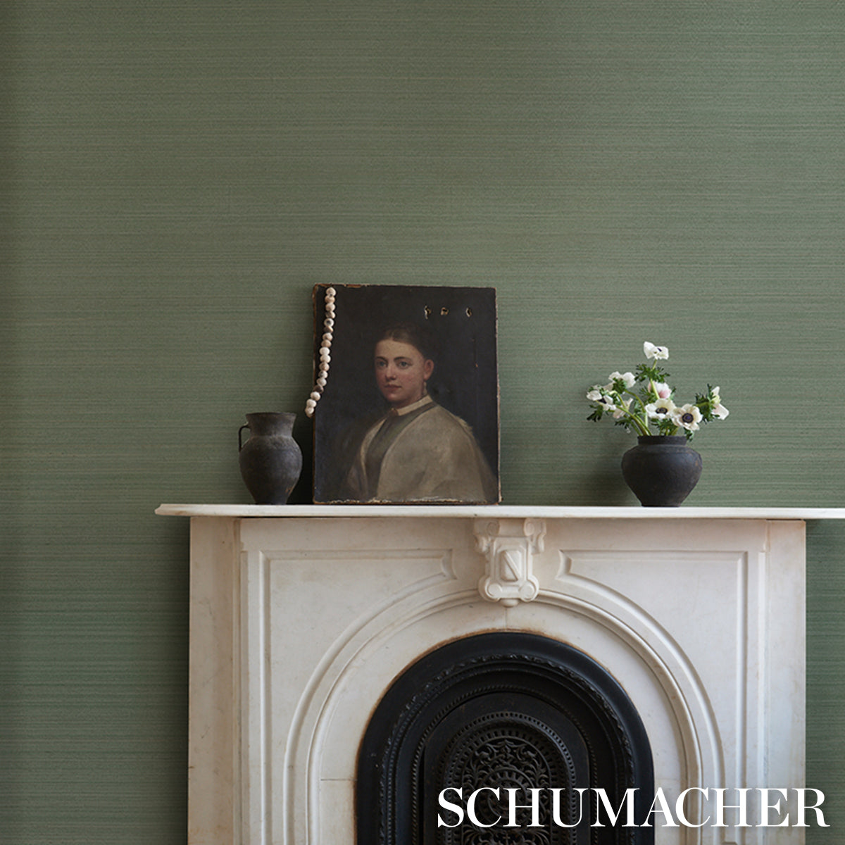 White marble mantel with arch, black insert; green textured wall, dark vases, leaning portrait with pearls, white flowers.
