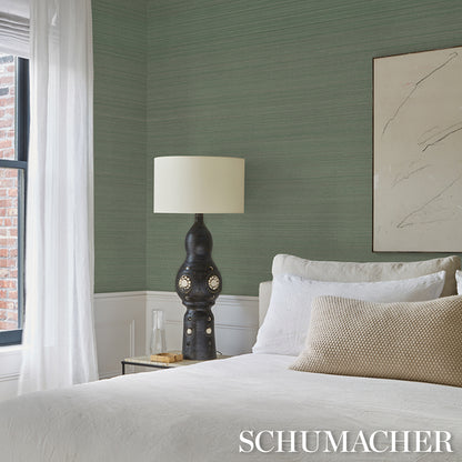 Dark ceramic table lamp with circular cutouts on a nightstand beside white bedding and a green textured wall.
