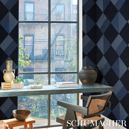 Bright room with blue diamond wallpaper, large window, stone table, cane-back chair, ceramic vase, bowls and books.