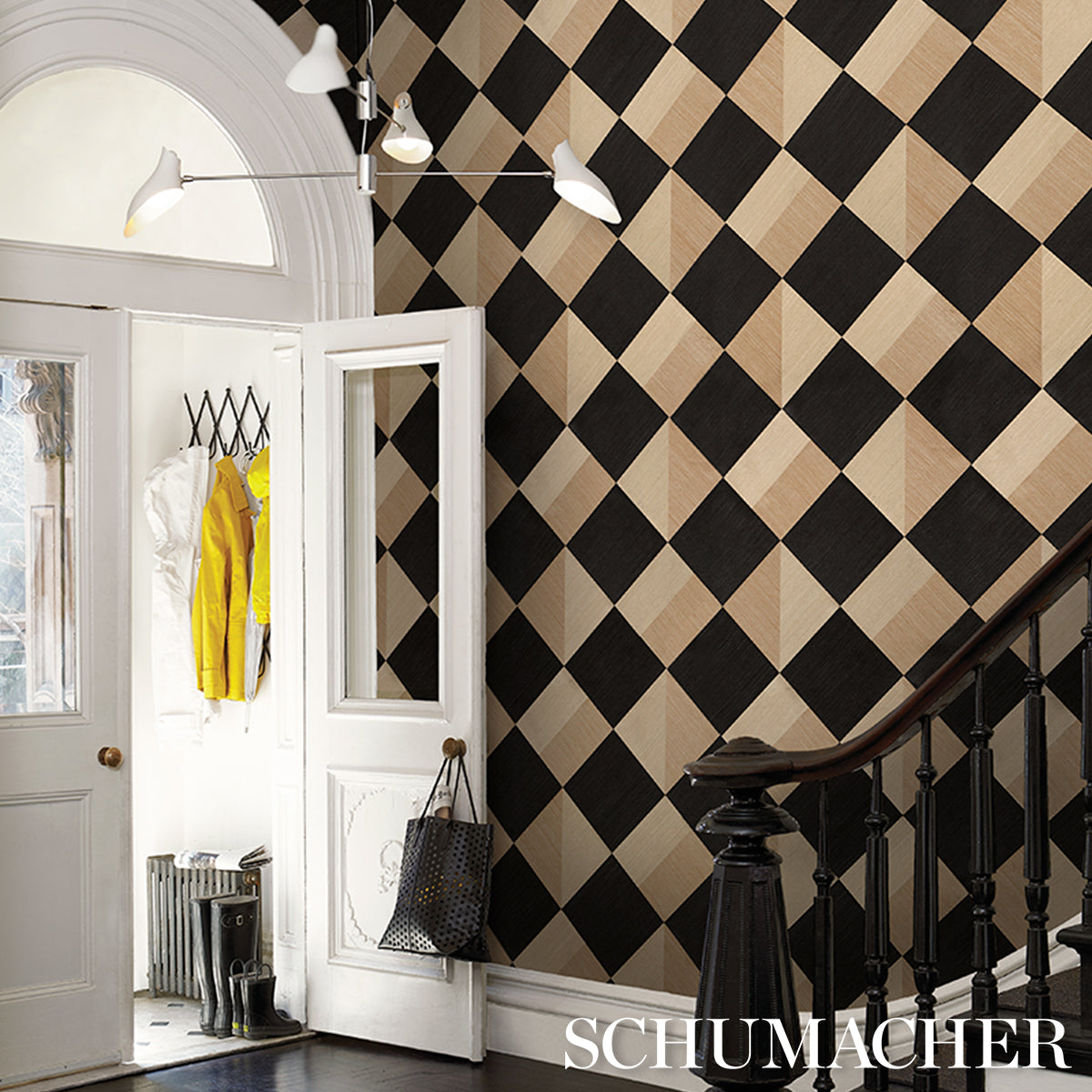 Harlequin black and beige diamond wallpaper in an entry hall, with white doors, a staircase railing, and a coat.