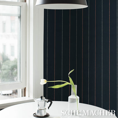 Dark navy striped wallpaper with thin red lines, white round table, moka pot, and tulip in glass vase under a pendant lamp.