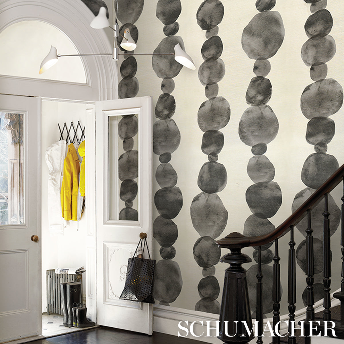 Entryway with grayscale bead wallpaper, white doors, yellow coat, black handbag, and dark wooden staircase railing.