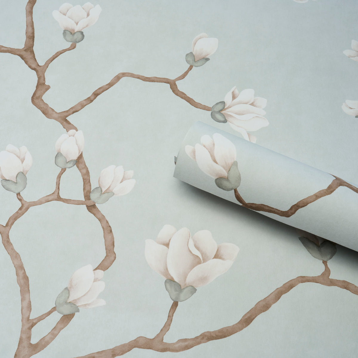 Soft blue wallpaper with brown tree branches and white magnolia blossoms; roll partially unrolled.