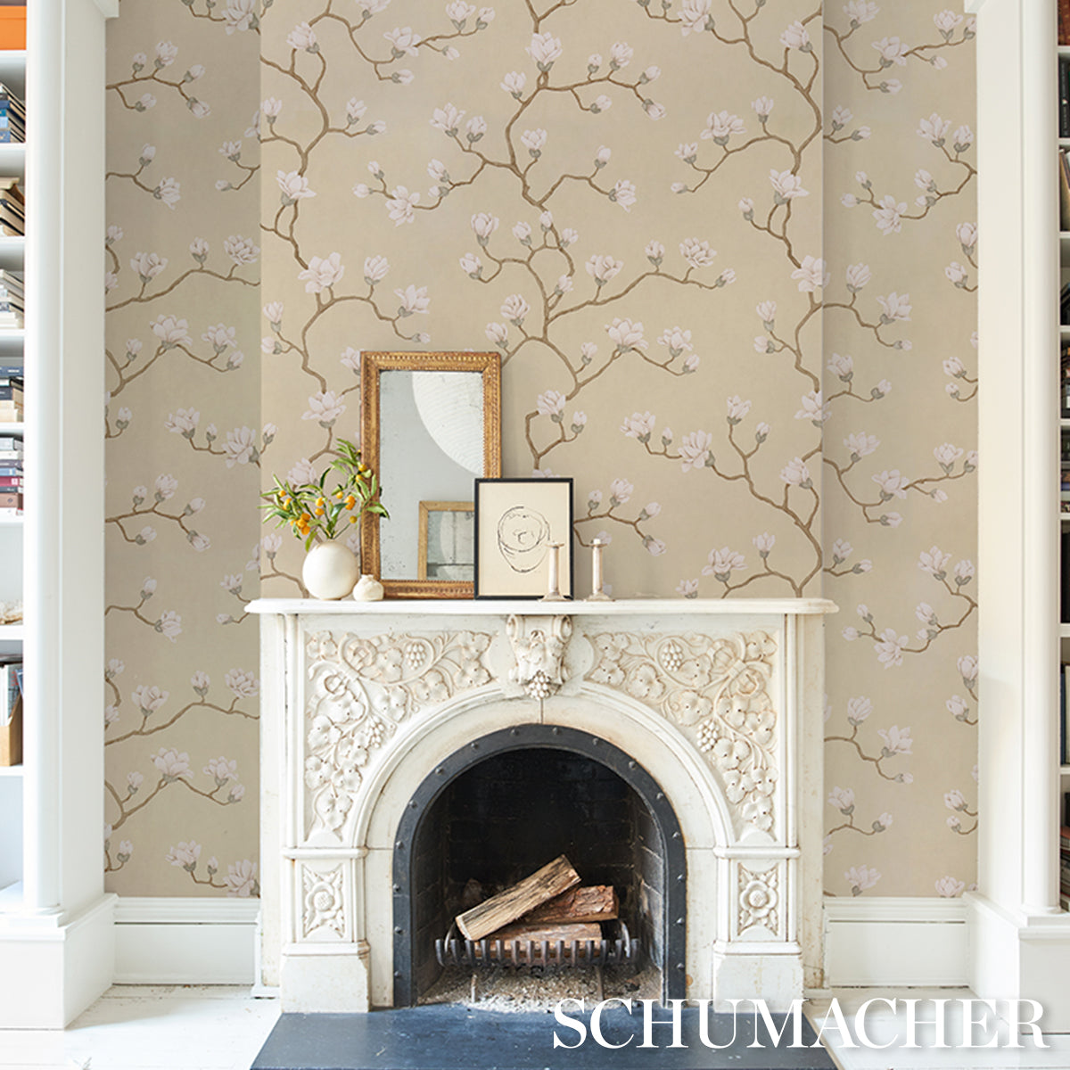 Beige wallpaper with pink blossom branches above a white ornate mantel in a bright living room.