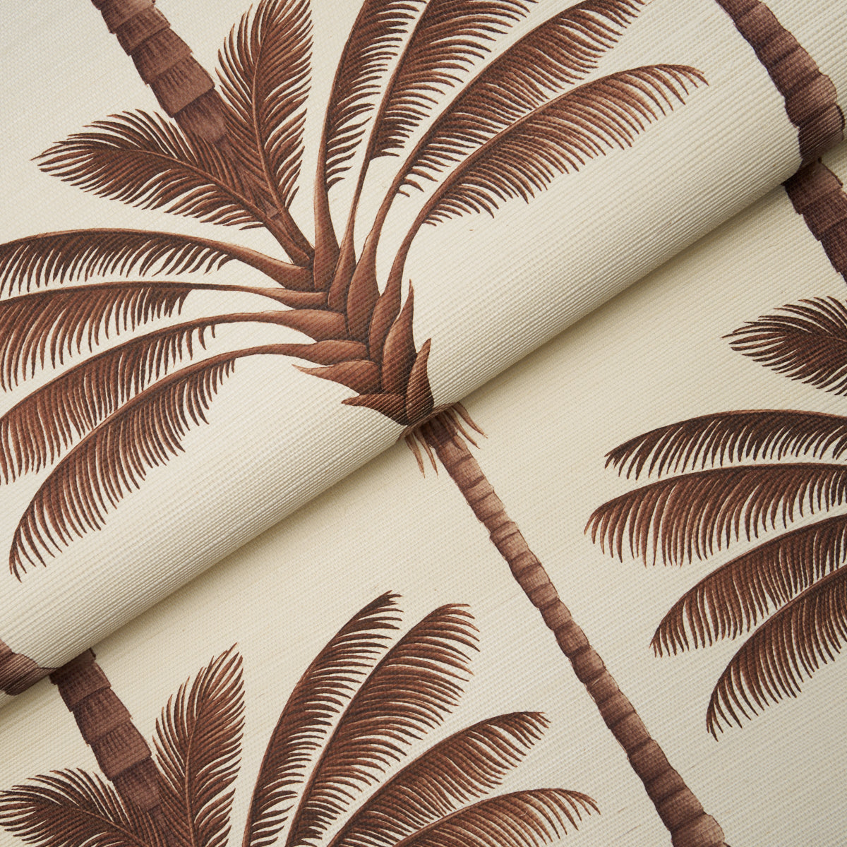 Beige fabric with brown palm tree print, rolled at the edge, tropical foliage suitable for upholstery or curtains.