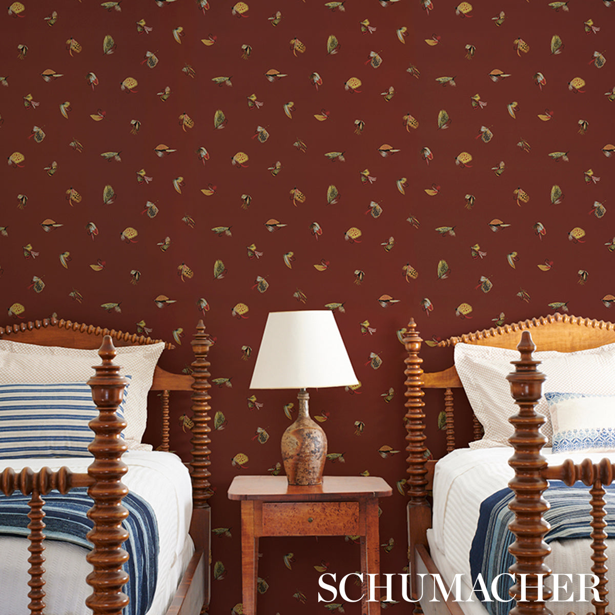 Ornate dark-wood four-poster beds with white linens and blue striped throws, carved bedside table and lamp, maroon wallpaper.