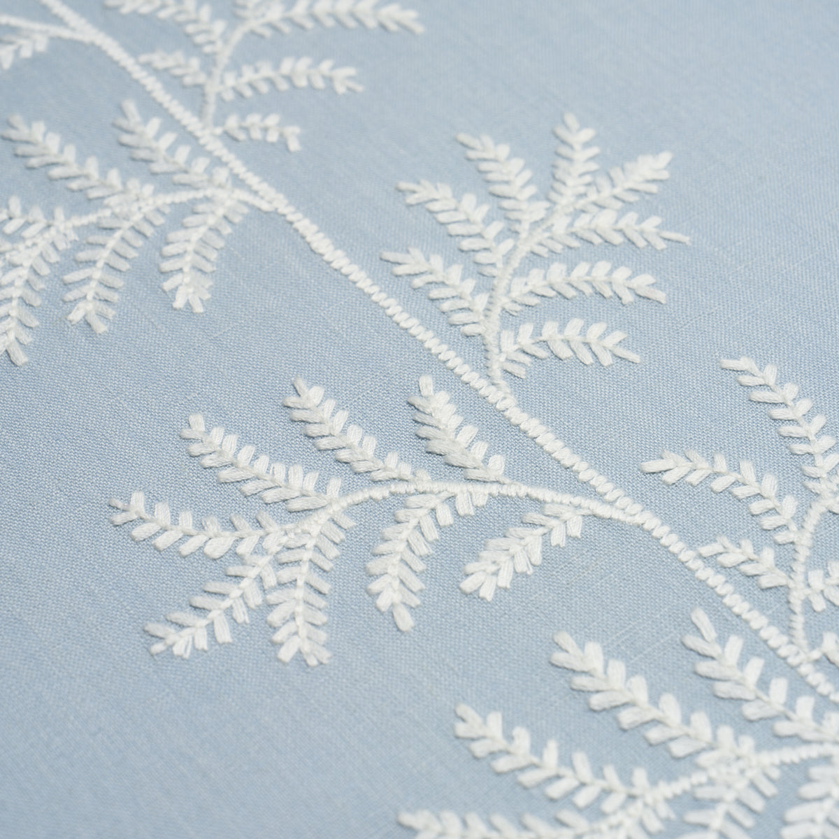 Light blue fabric with white embroidered fern-like branches across the surface.