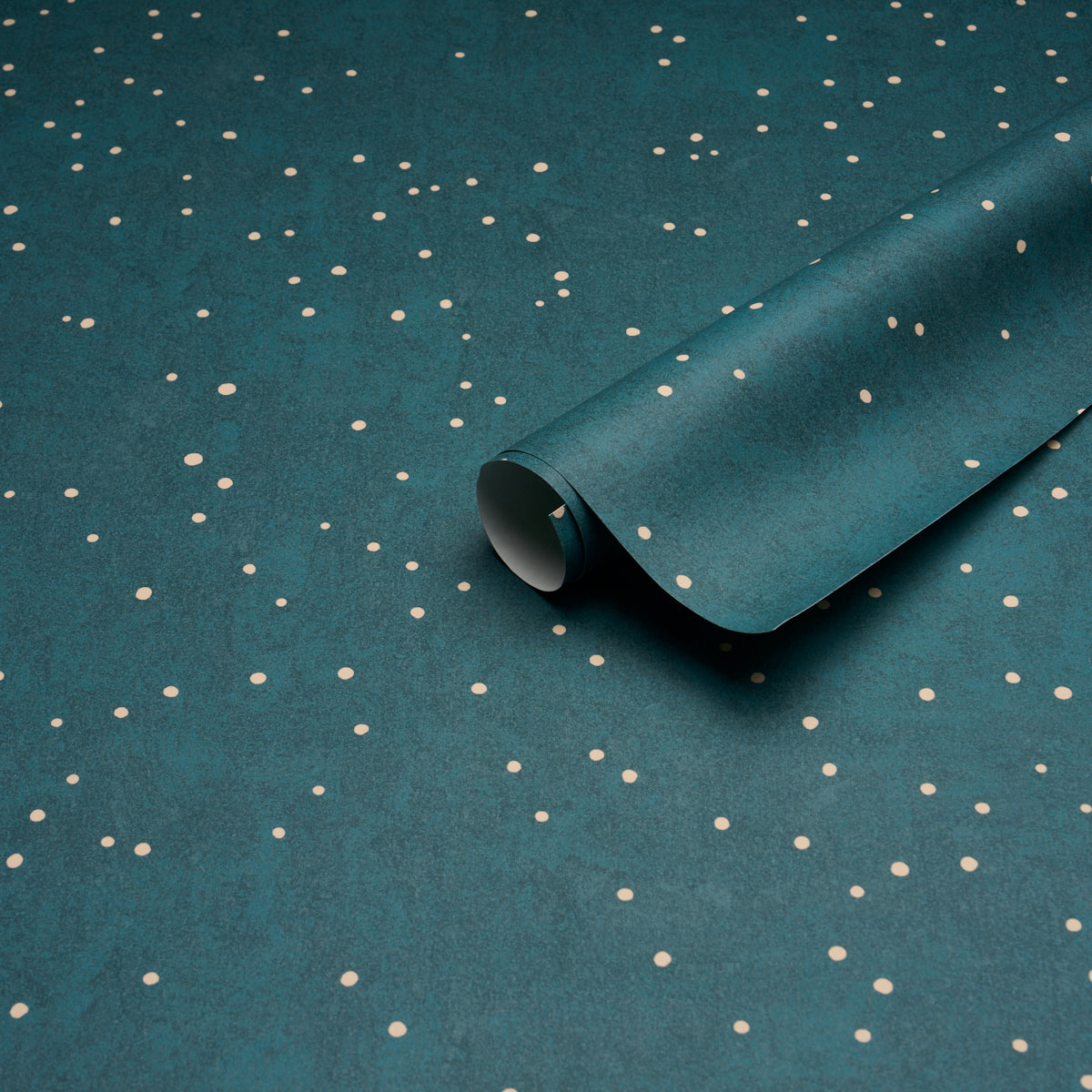 Teal wrapping paper with small white polka dots, partially rolled to reveal a curled edge.