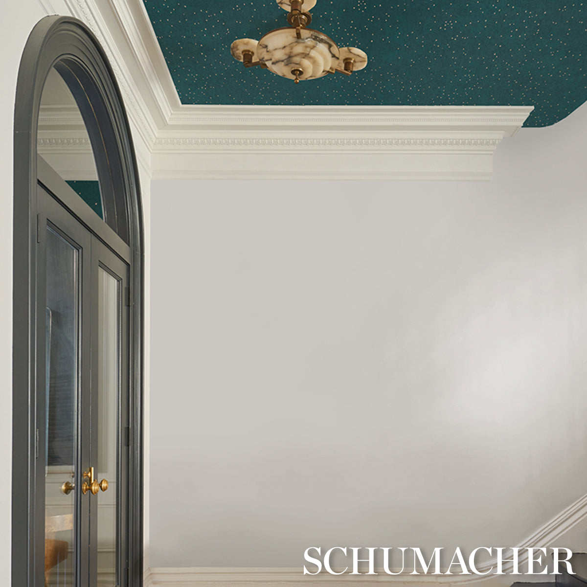 Luxurious interior with teal starry ceiling, white walls, crown molding, arched black glass door, brass chandelier.