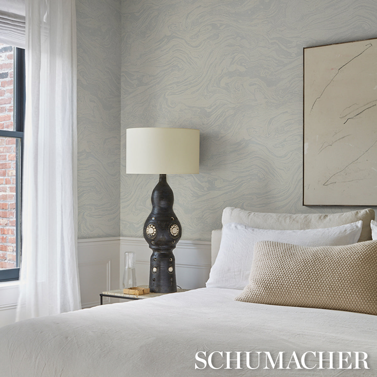 Bedroom with white linen, beige throw pillow, black sculptural lamp and cream shade, blue-gray wallpaper, abstract line art