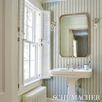 Vintage-style bathroom with pale green striped wallpaper, porcelain pedestal sink, brass-framed mirror.