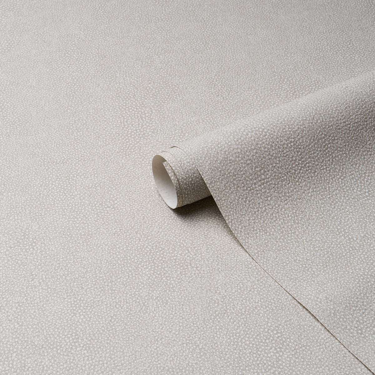 Beige dove textured vinyl with a tiny dot pattern and a rolled sheet visible for upholstery or drapery.