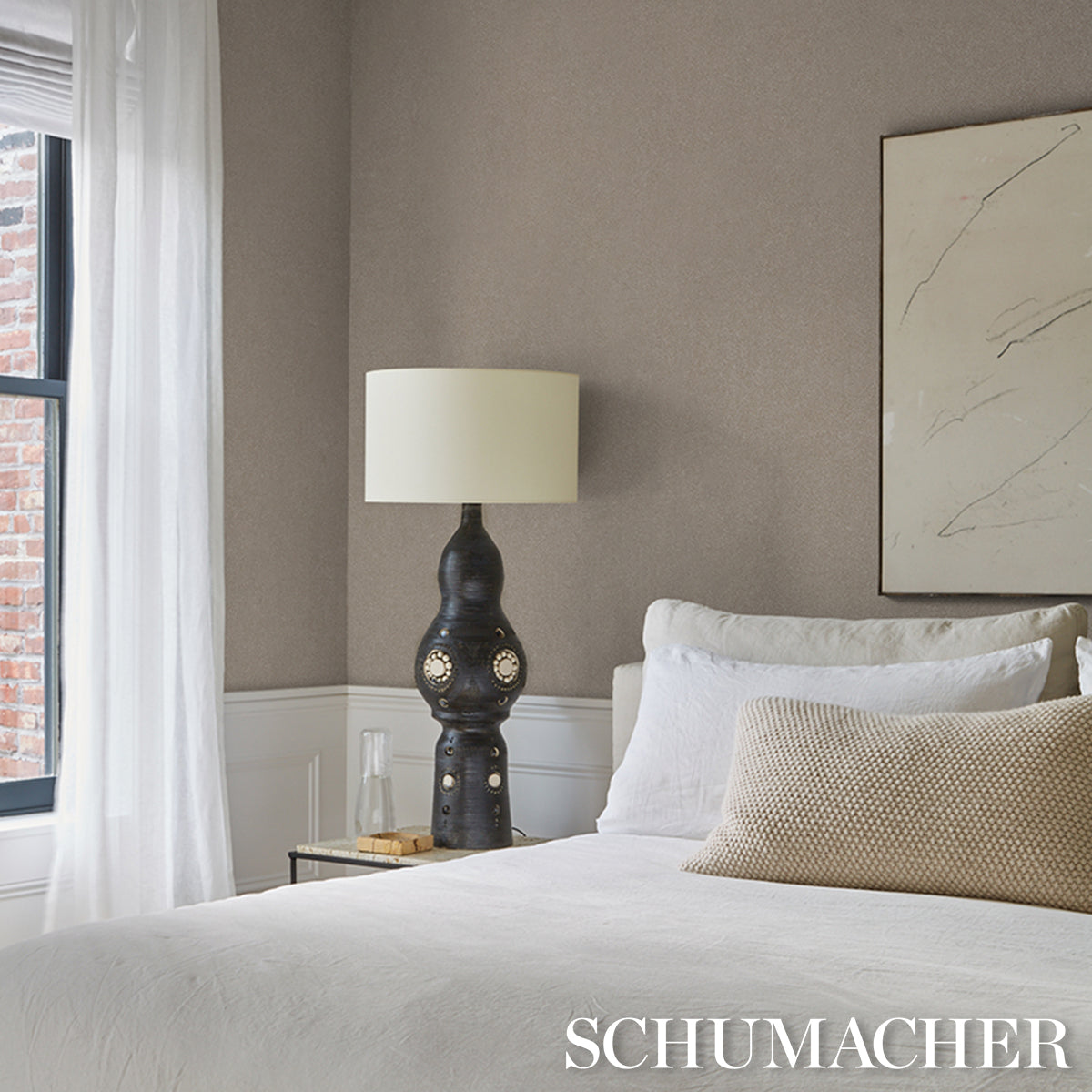 Neutral beige bedroom with white duvet, beige lumbar pillow, sculptural dark ceramic lamp with ivory shade, abstract wall art.