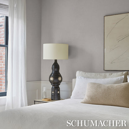 Modern bedroom with a sculptural dark lamp and beige shade, white bedding, beige throw pillow, glass nightstand, marble art.