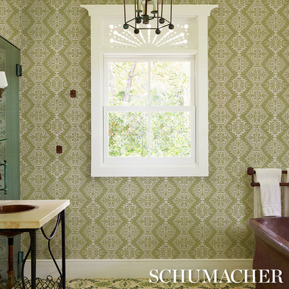 Green damask wallpaper in a vintage bathroom; white-framed window, brass fixtures, sink and tub.