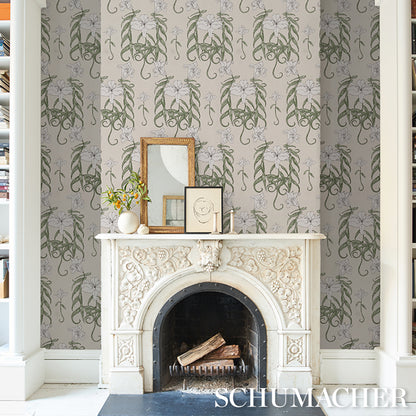 Ornate white carved fireplace with logs; grey-green damask wallpaper; mantel displays framed art & a vase.