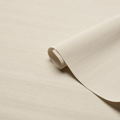 Beige textured wallpaper roll curling at the edge on a pale wood surface.