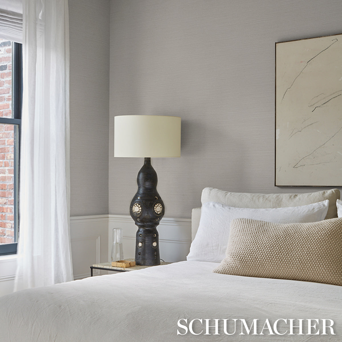 Modern bedroom with white bedding, beige throw pillow, sculptural ceramic lamp with shade, glass side table, abstract art.