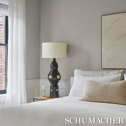 Modern bedroom with white bedding, beige throw pillow, sculptural ceramic lamp with shade, glass side table, abstract art.