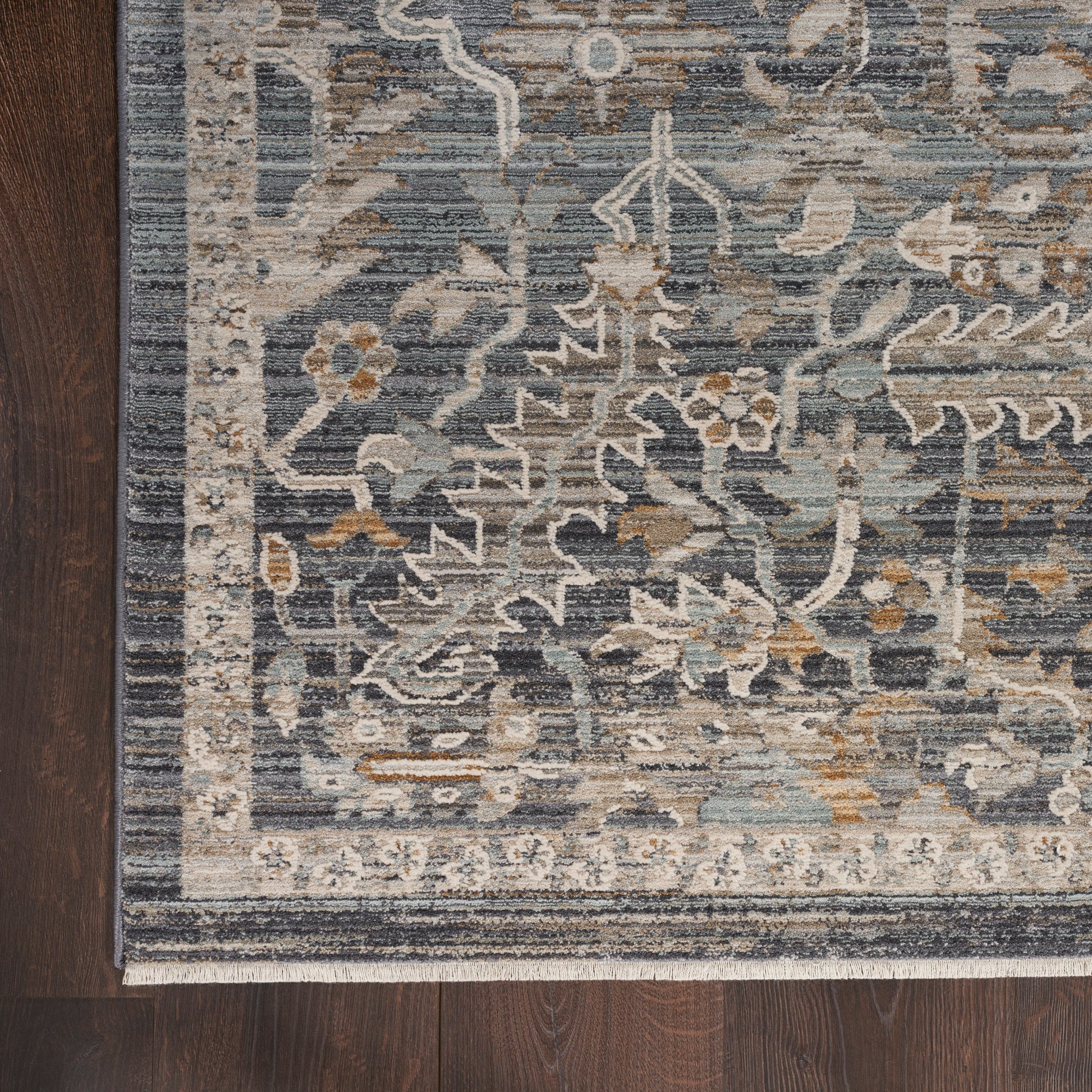 Navy blue and gray floral oriental rug with beige accents and a fringed border on dark hardwood floor.