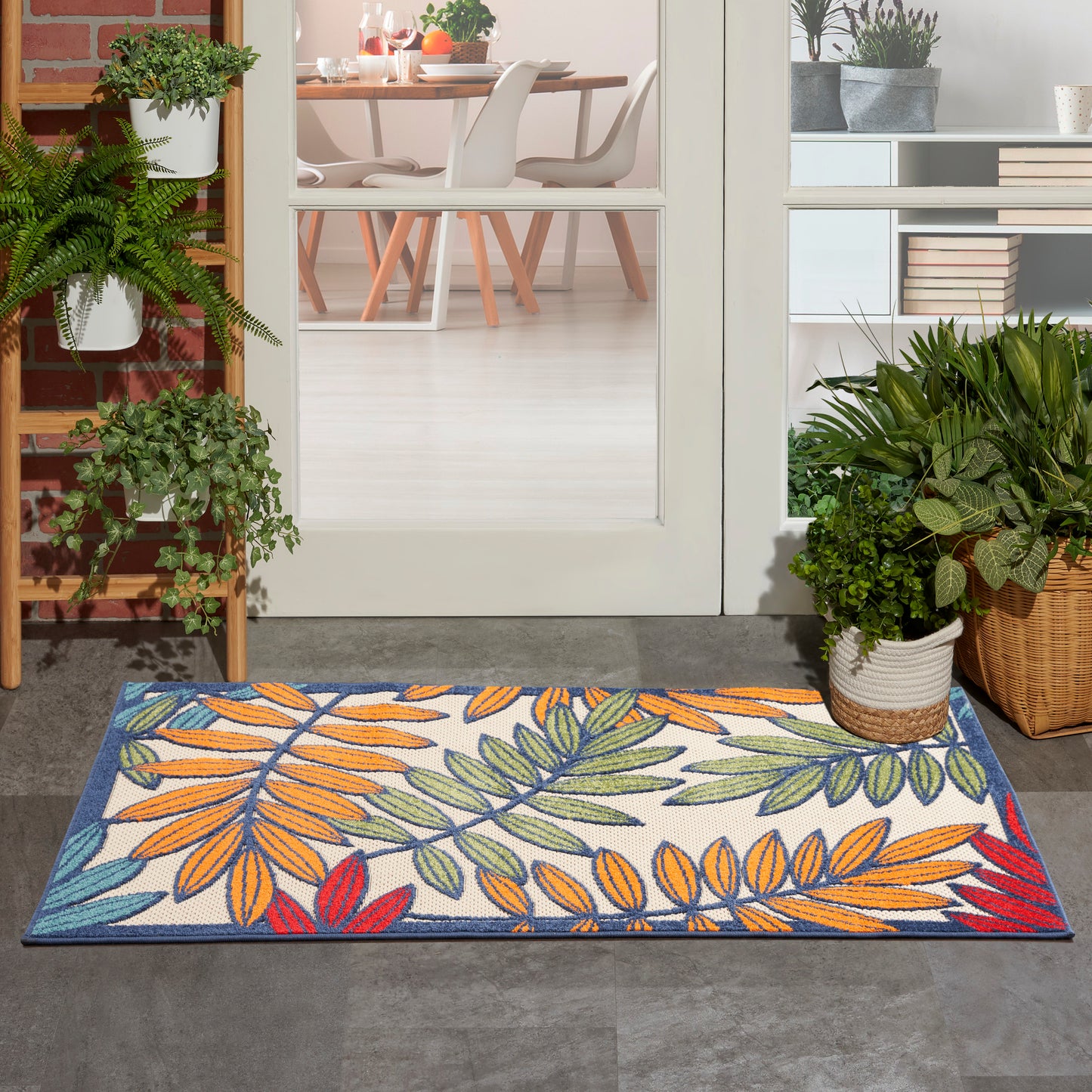 Colorful leaf-pattern rug at doorway with orange, green and blue leaves; potted plants and dining room visible inside.