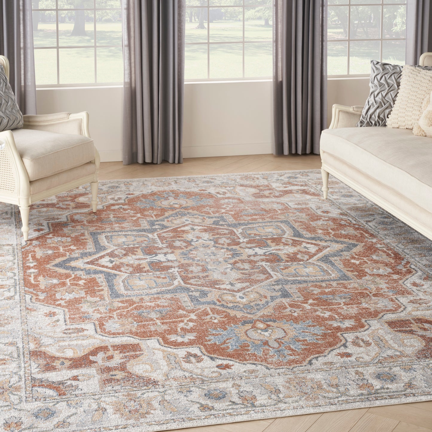 Living room with a large orange, blue and ivory oriental rug, beige sofas and armchairs, gray curtains.