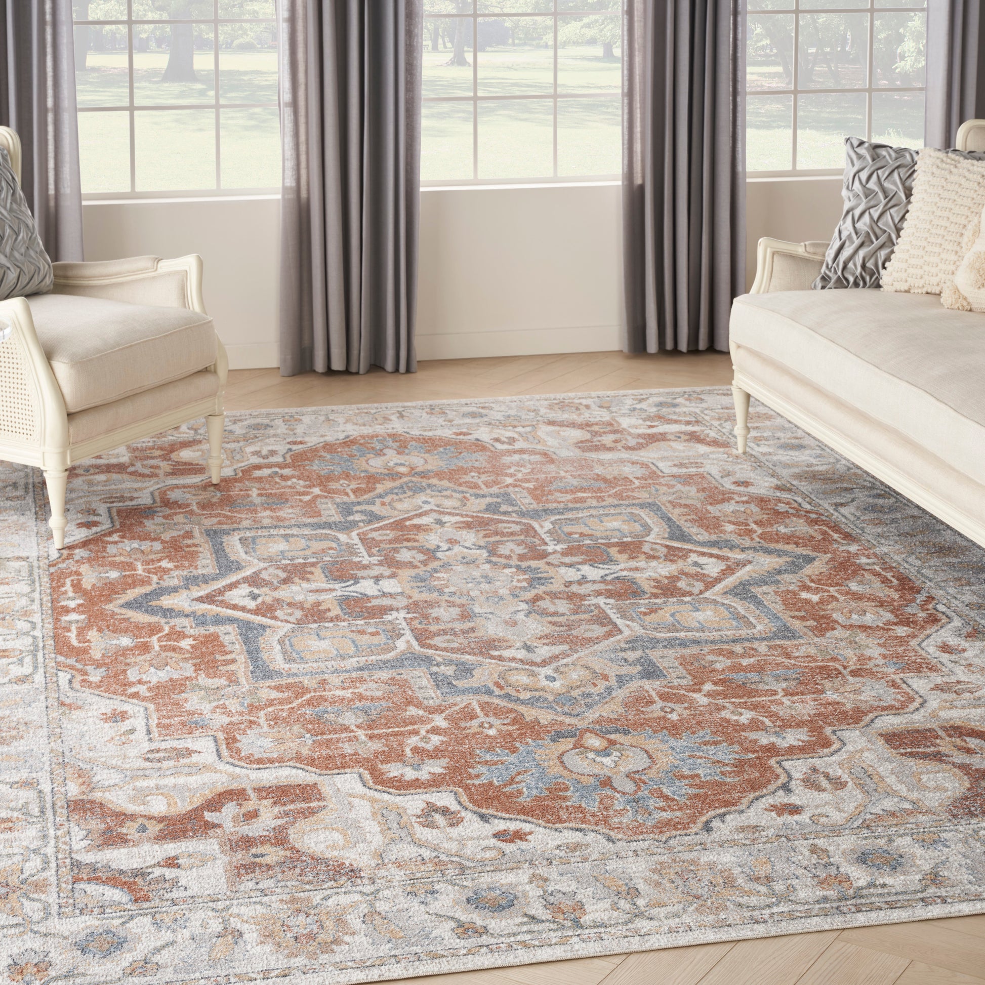 Living room with a large orange, blue and ivory oriental rug, beige sofas and armchairs, gray curtains.