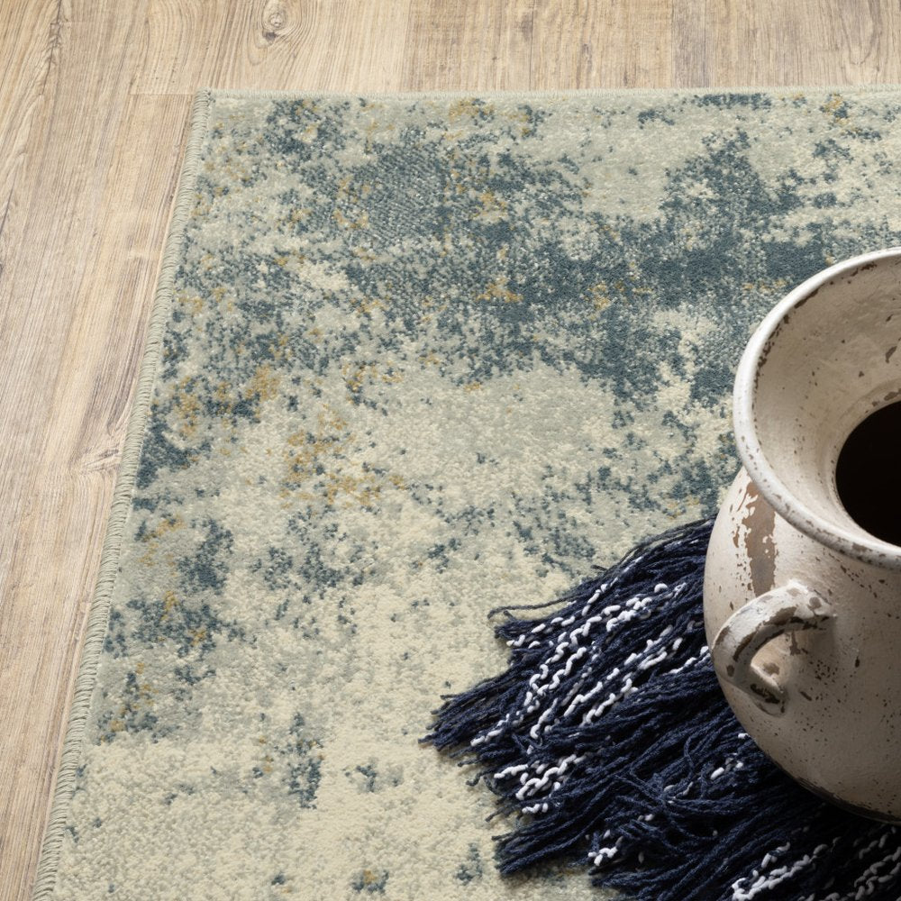 Beige, teal, grey and gold abstract area rug with fringe on wood floor.