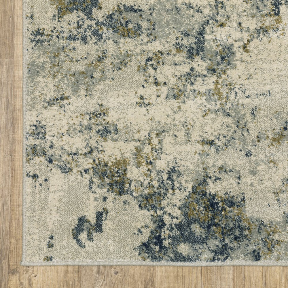 Rectangular abstract area rug with beige base, blue & gray & gold splotches, light border on wood floor.