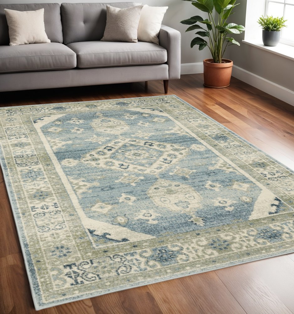 Blue and ivory oriental area rug with floral border on hardwood floor beside a grey sofa and potted plant.