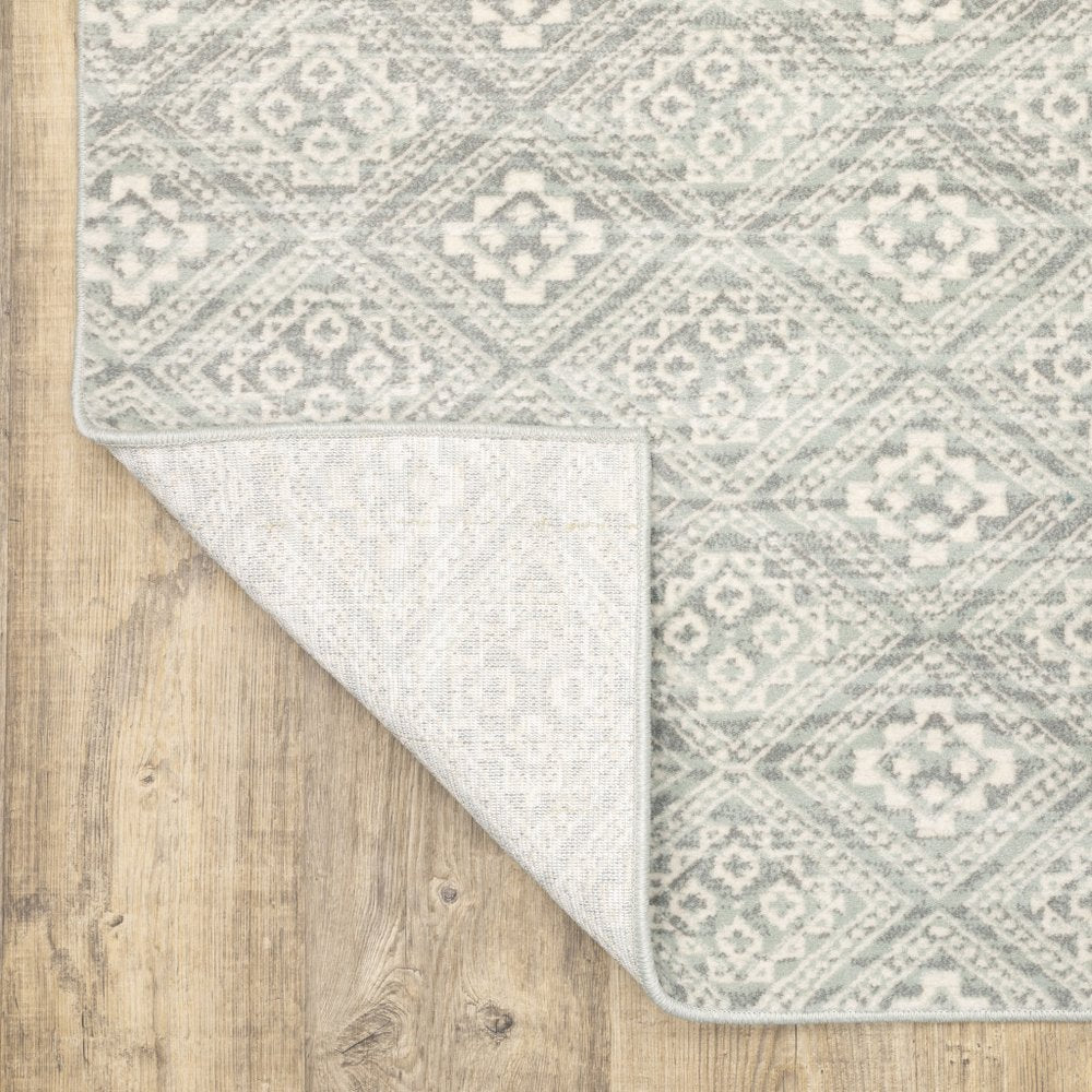 Light gray and gray geometric distressed area rug on wood floor; corner folded to reveal light underside.
