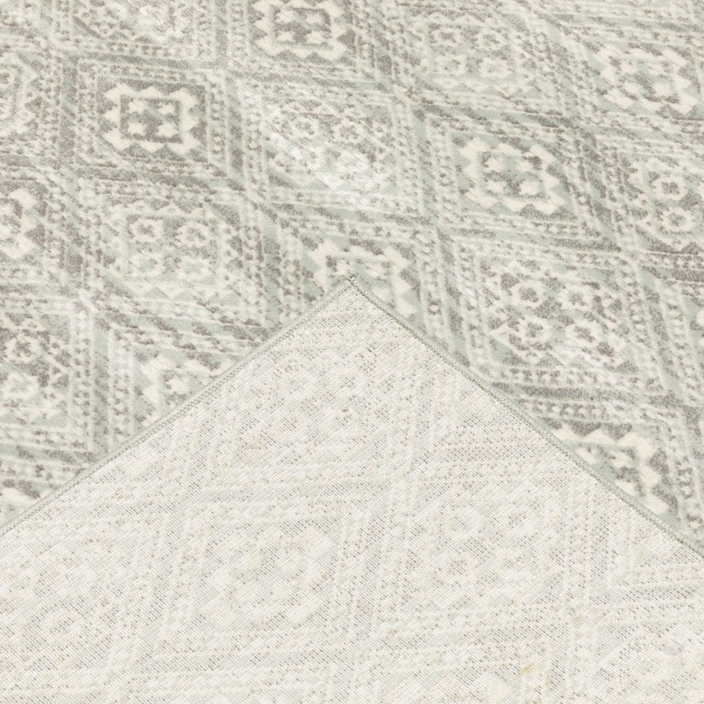 Two-tone woven area rug with geometric distressed motifs in light gray and gray; corner folded to reveal a lighter overlay.