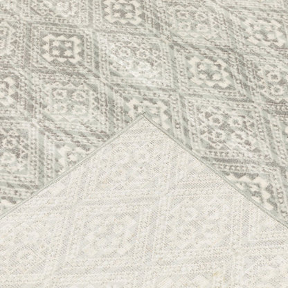 Two-tone woven area rug with geometric distressed motifs in light gray and gray; corner folded to reveal a lighter overlay.