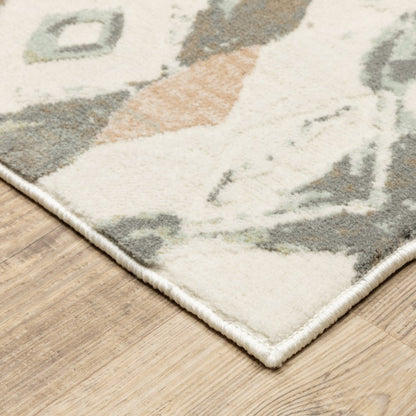 Ivory pink and sage geometric area rug with a fringed edge on a wood floor.