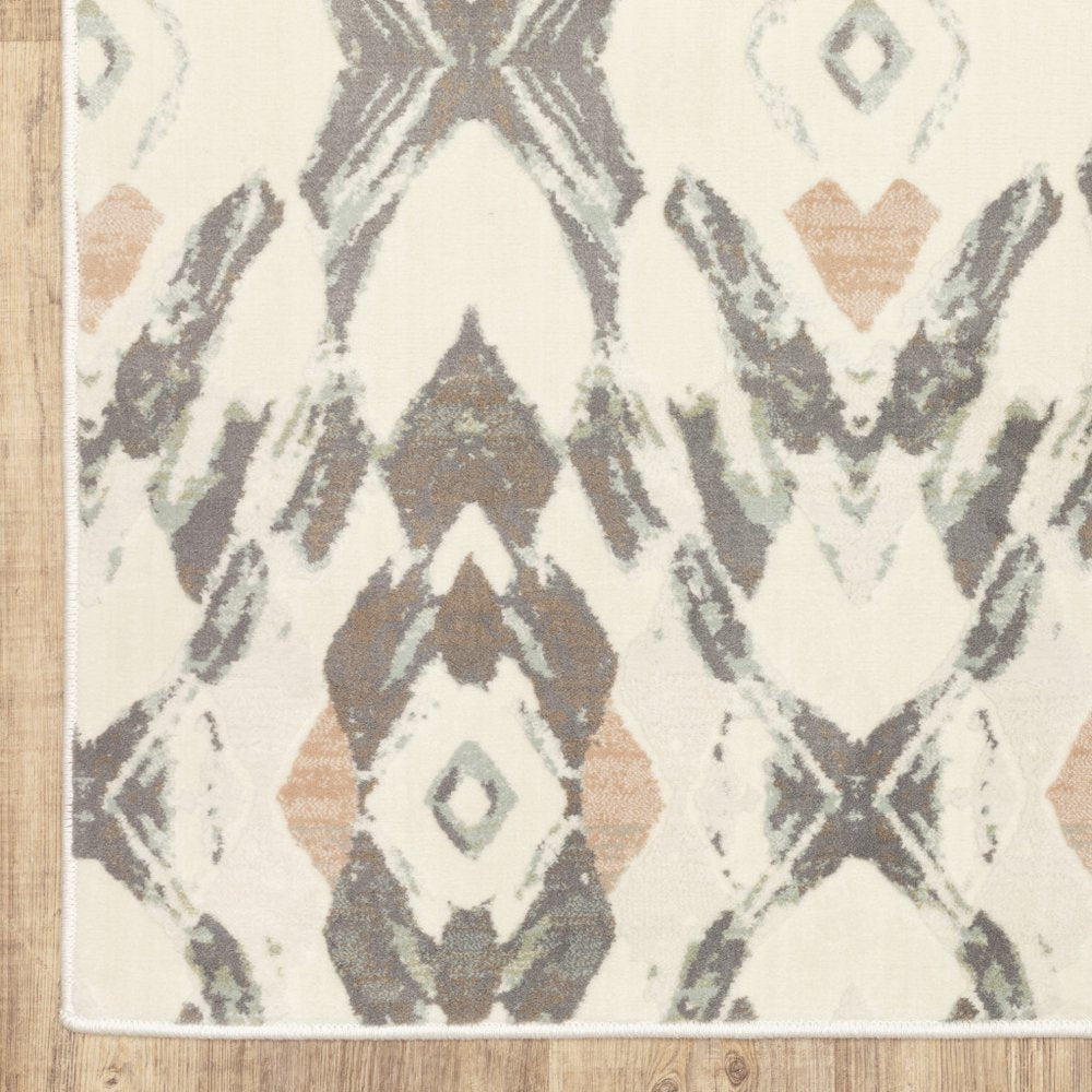 Ivory pink and sage geometric ikat diamond pattern area rug on wood floor.
